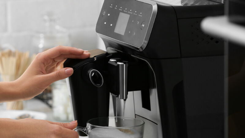 Woman using modern espresso machine for making coffee with milk